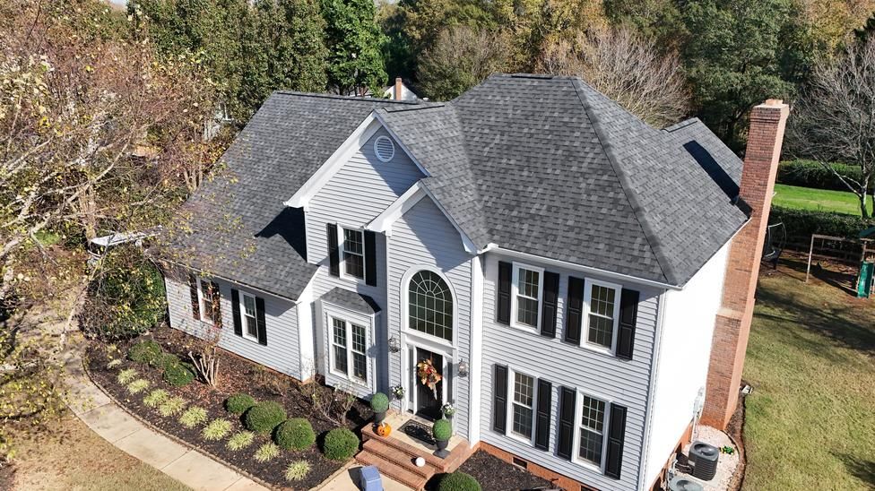 Aerial view of a white two-story house with a dark gray roof, black shutters, and a landscaped front yard.