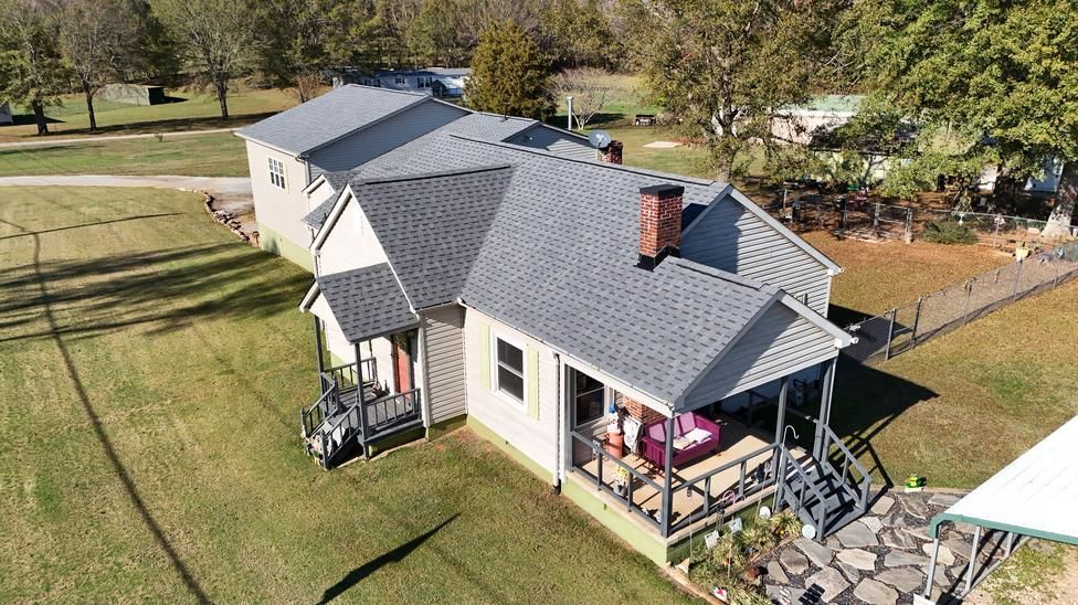 Aerial view of a white house with a gray roof, porch, and surrounding lawn on a sunny day