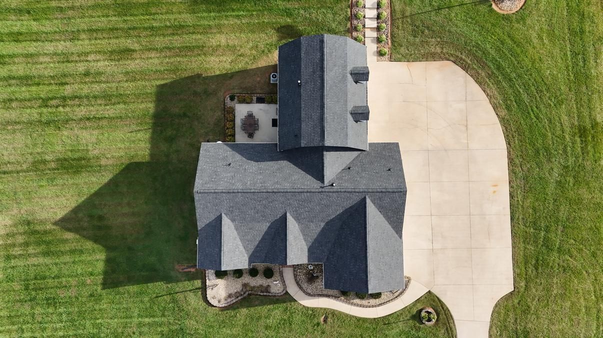Aerial view of a gray-roofed house with a large driveway and green lawn.