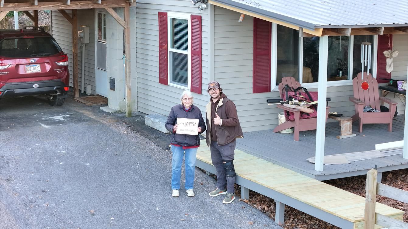 Two people standing outside a house, one holding a sign, with a red car and porch swing nearby.