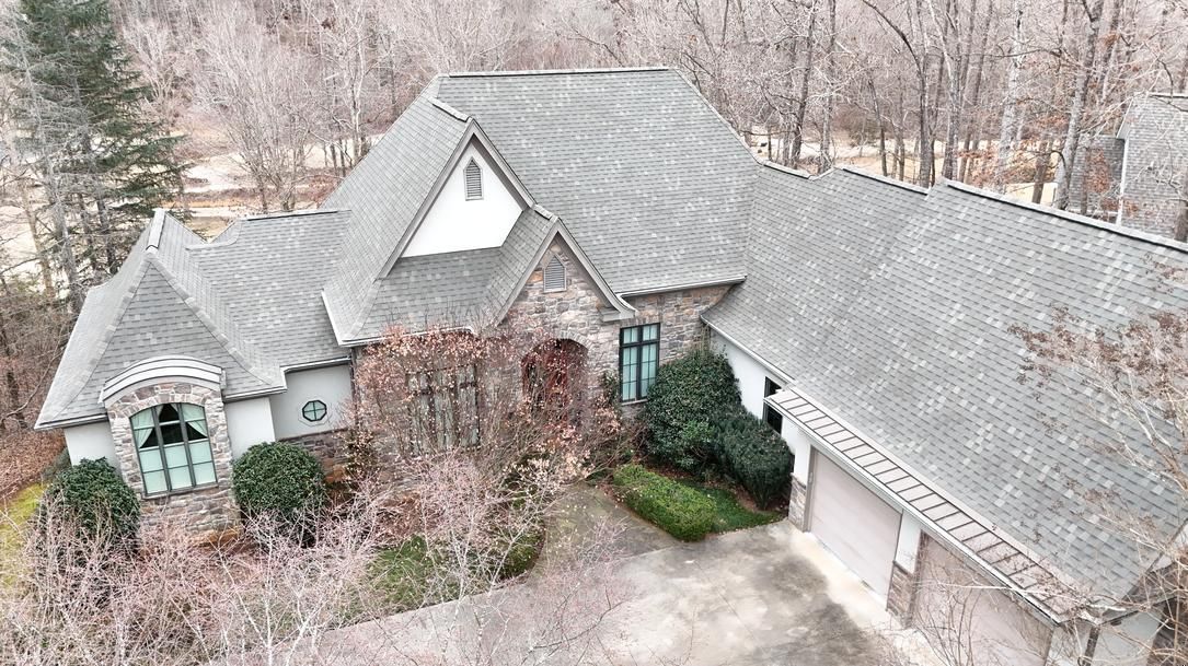 Aerial view of a large gray-roofed suburban house surrounded by leafless trees and shrubs