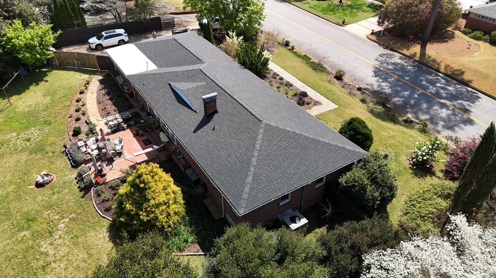 Aerial view of a suburban house with a dark roof, garden, driveway, and street nearby