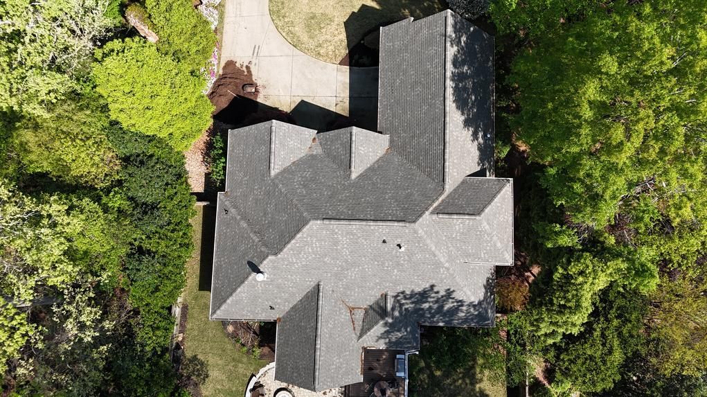 Aerial view of a gray-roofed house surrounded by dense green trees and a winding driveway.