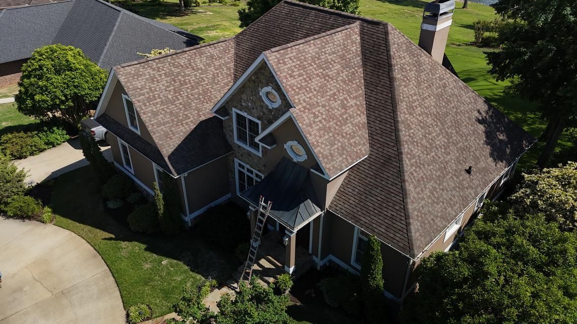 Aerial view of a gray-roofed suburban house with a driveway and surrounding trees