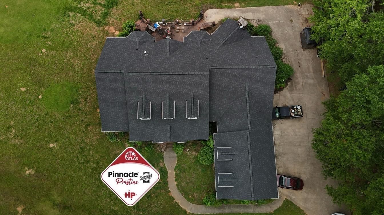 Aerial view of a dark-roofed house with driveway, parked cars, and a Pineapple Studio sign on the lawn.