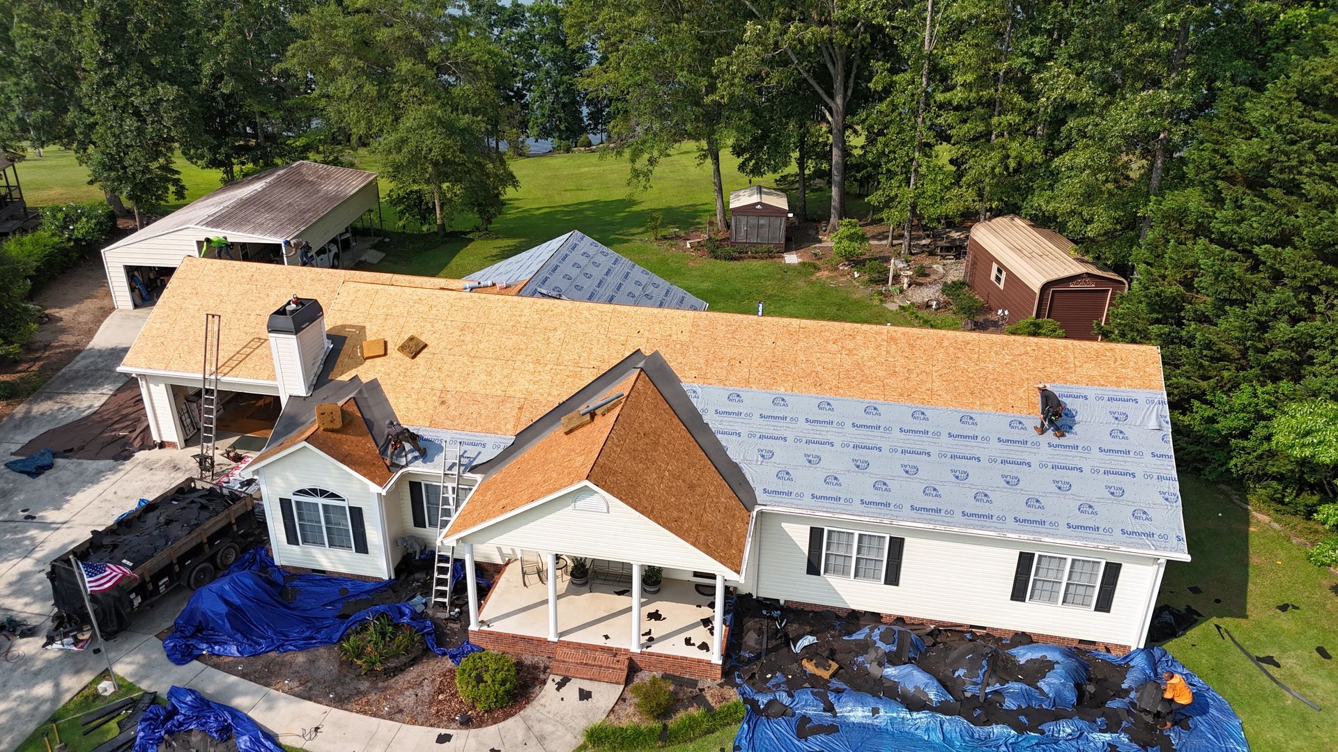 House under roof repair with exposed plywood and blue tarps in a wooded residential area