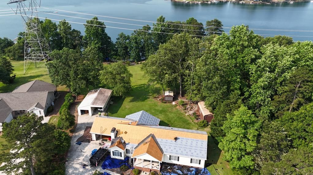 Aerial view of lakeside homes with trees, a dock, and a calm blue body of water beyond.