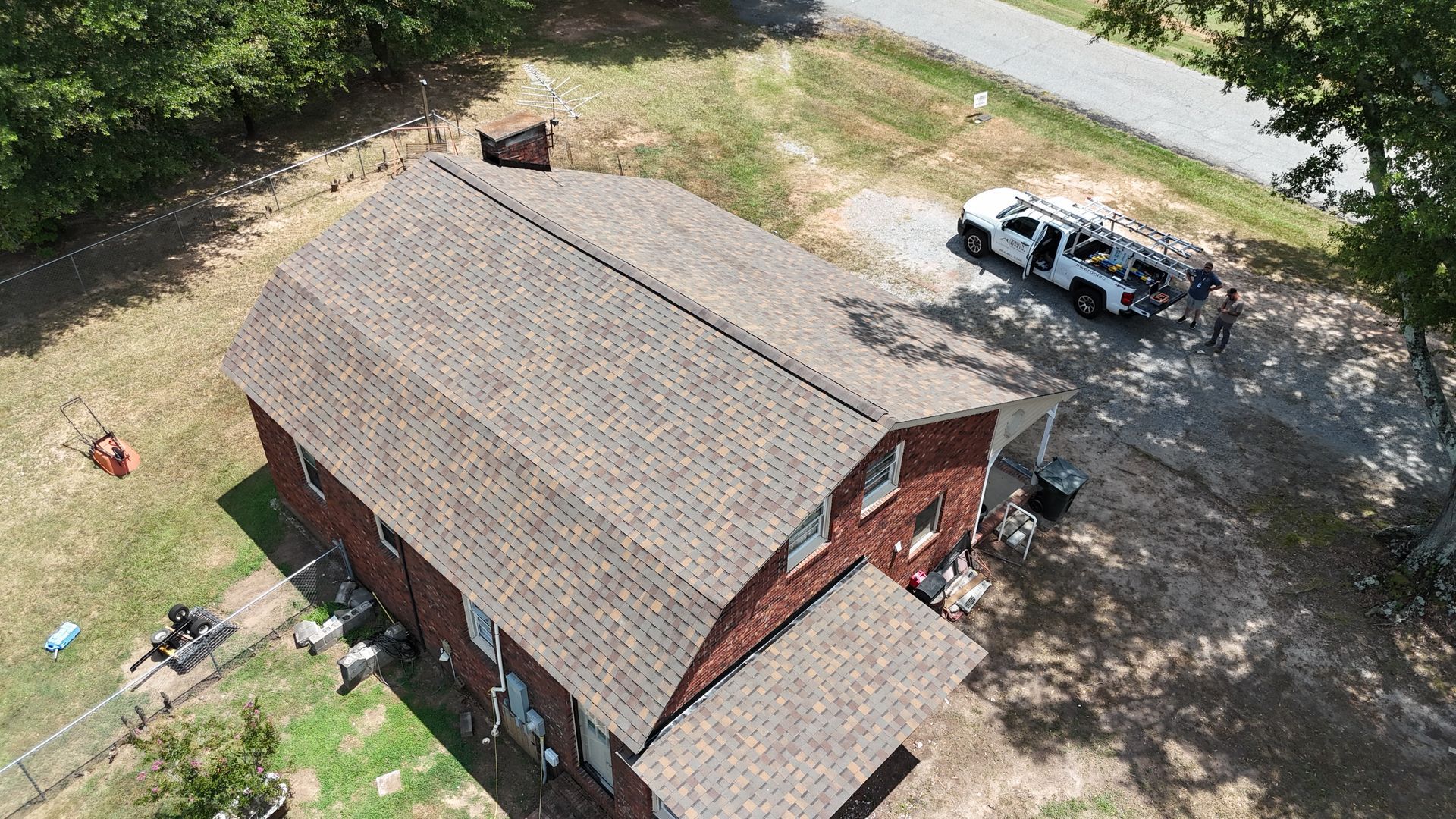 Aerial view of a red brick house with a shingled roof and a white pickup truck in the driveway.