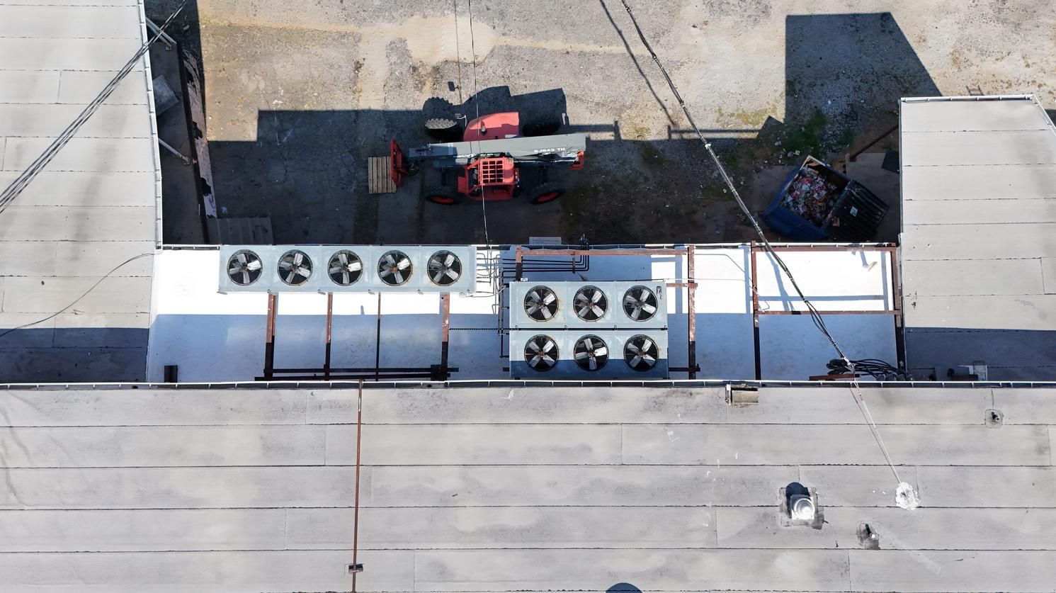 Rooftop HVAC units and ductwork beside two red vehicles in a fenced industrial area