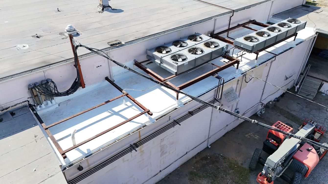 Aerial view of rooftop HVAC units and ductwork on a commercial building, with parked trucks below.