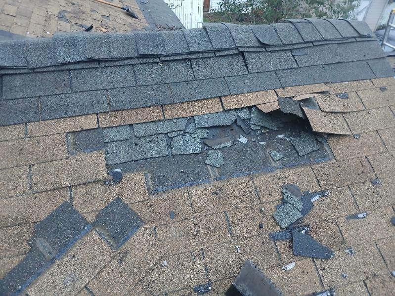Damaged shingle roof with a large hole and scattered debris on the surface