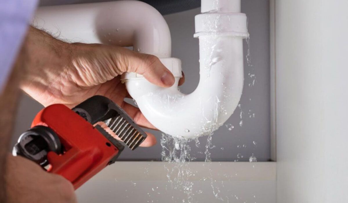 a man's hands using a pipe wrench to repair a leaking pipe