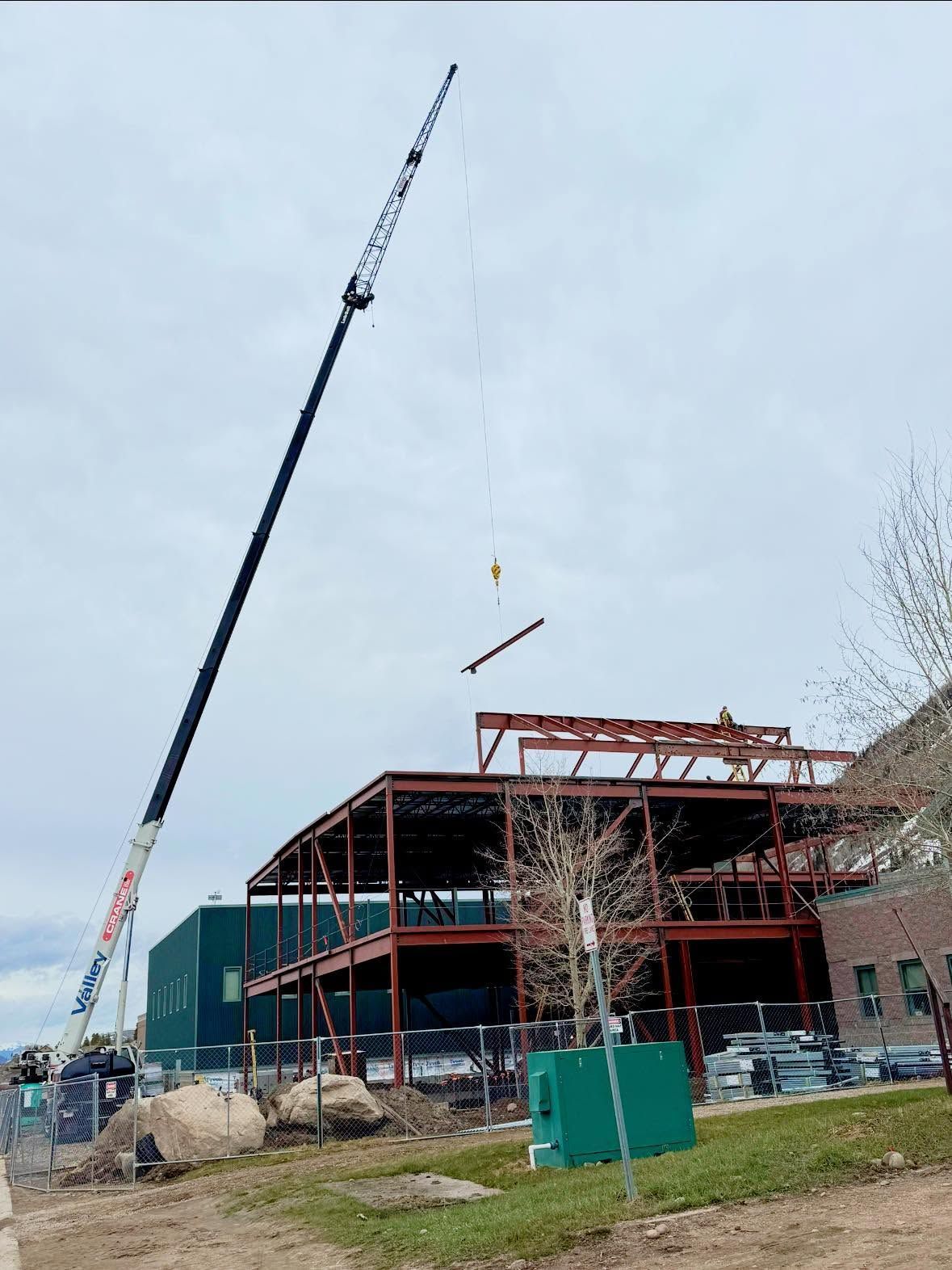 Crane lifting steel beams for a building under construction with a red frame and green siding