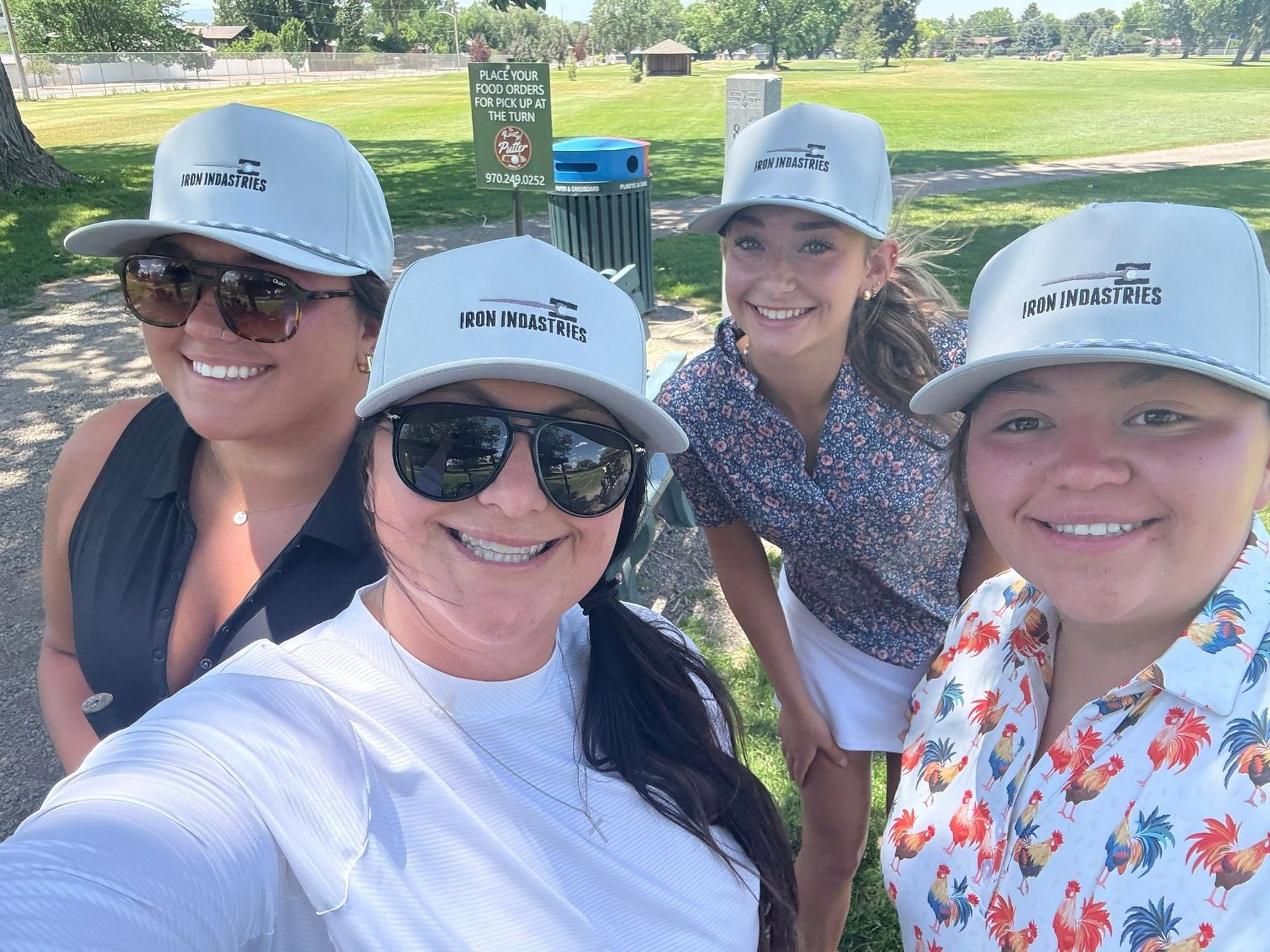 Four smiling friends in gray hats posing for a selfie in a sunny park