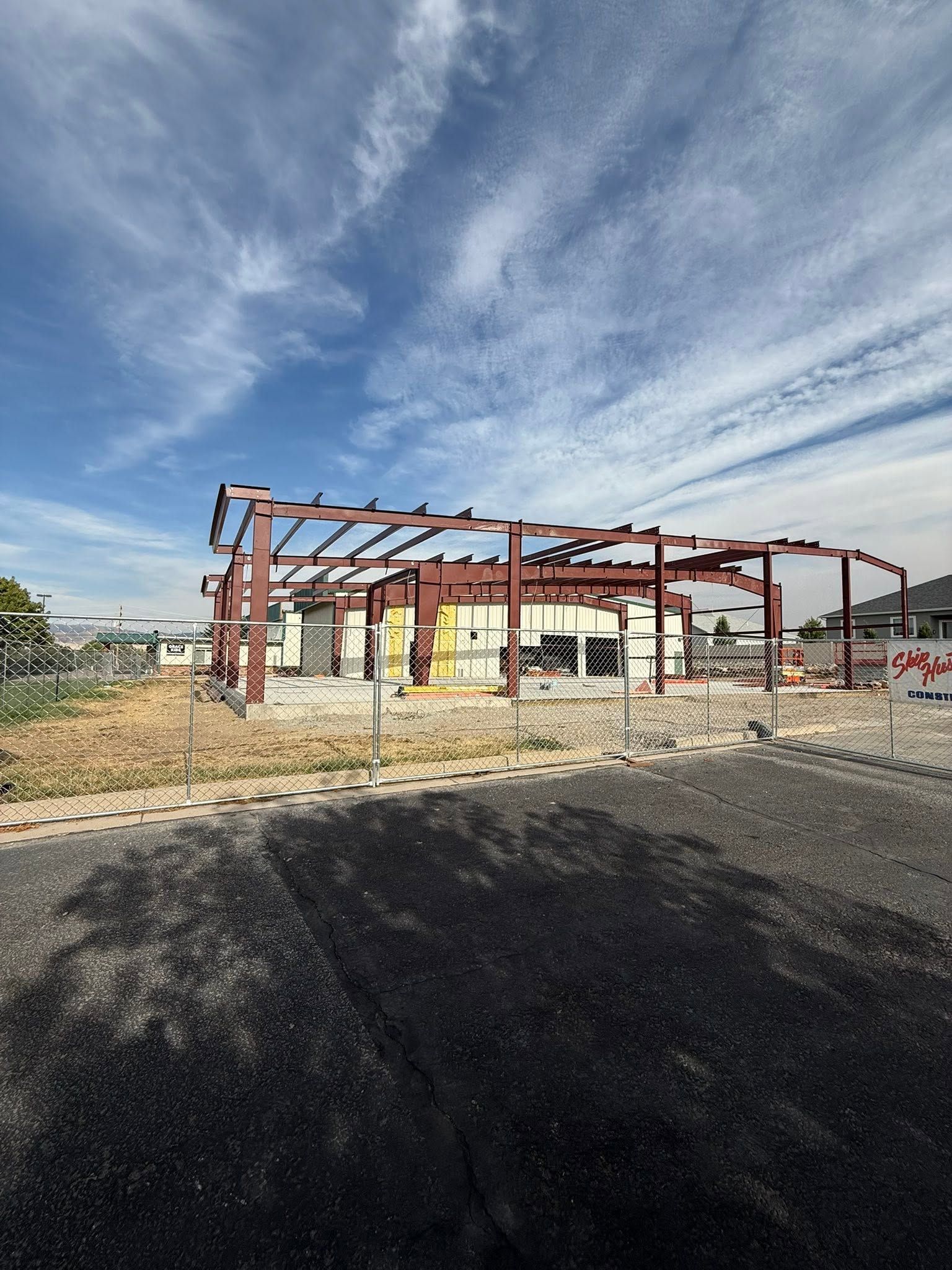 Construction site with red steel frame under a blue sky and a dark gravel foreground