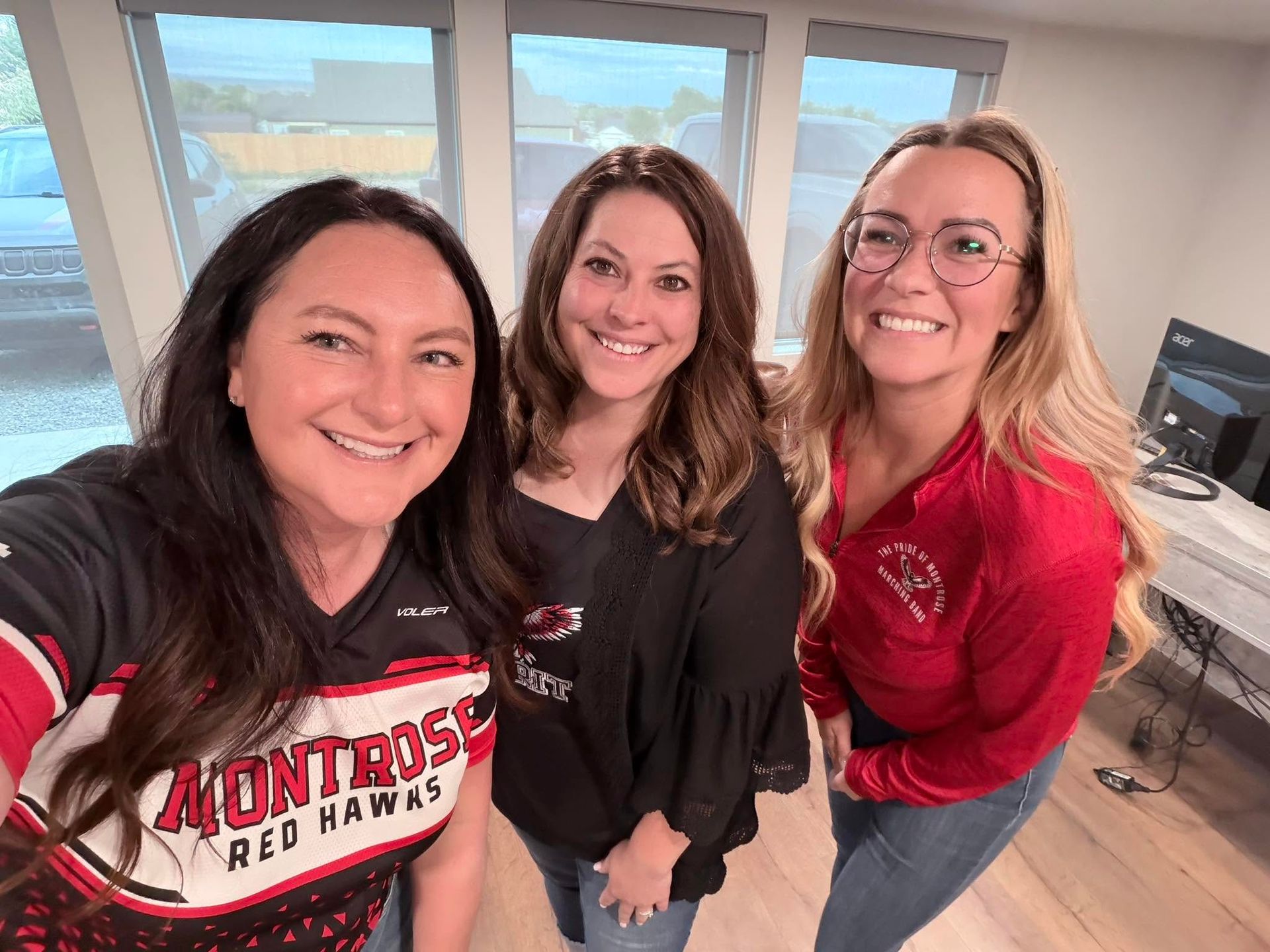 Three smiling women posing indoors, wearing black and red Northrose Hawks shirts.