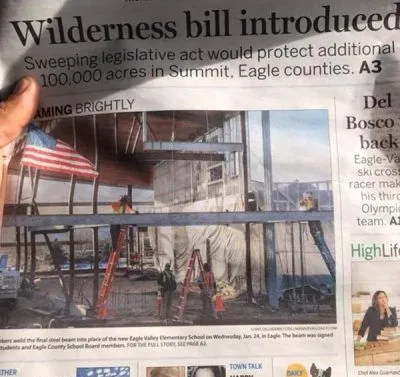 Newspaper front page showing wildfire damage and a building under construction with an American flag