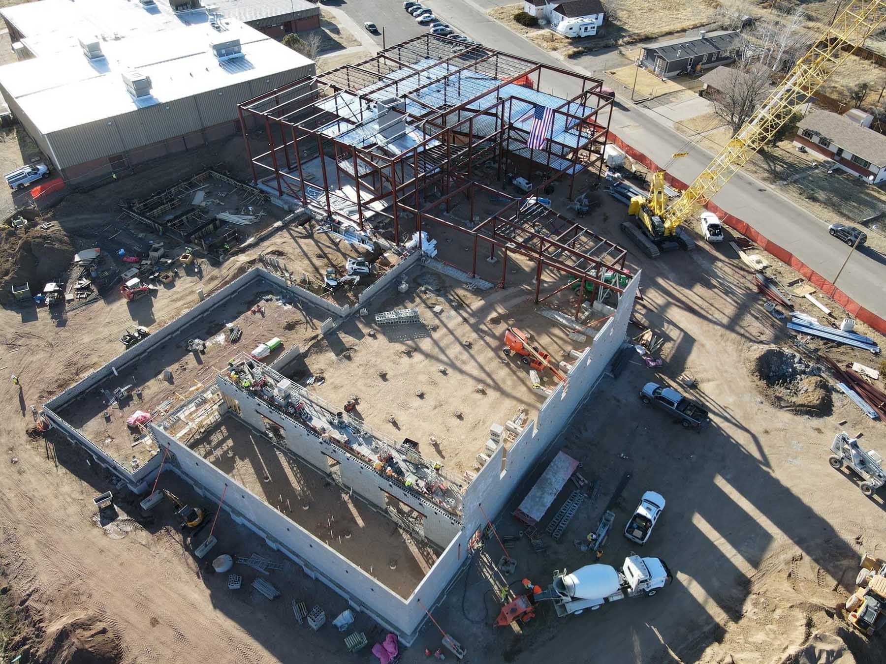 Aerial view of a building under construction with steel framing, concrete walls, and construction vehicles.