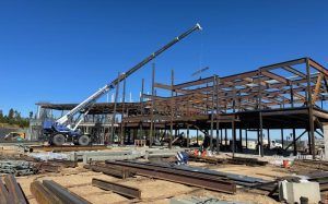 Construction site with steel frame building and crane lifting materials under a clear blue sky