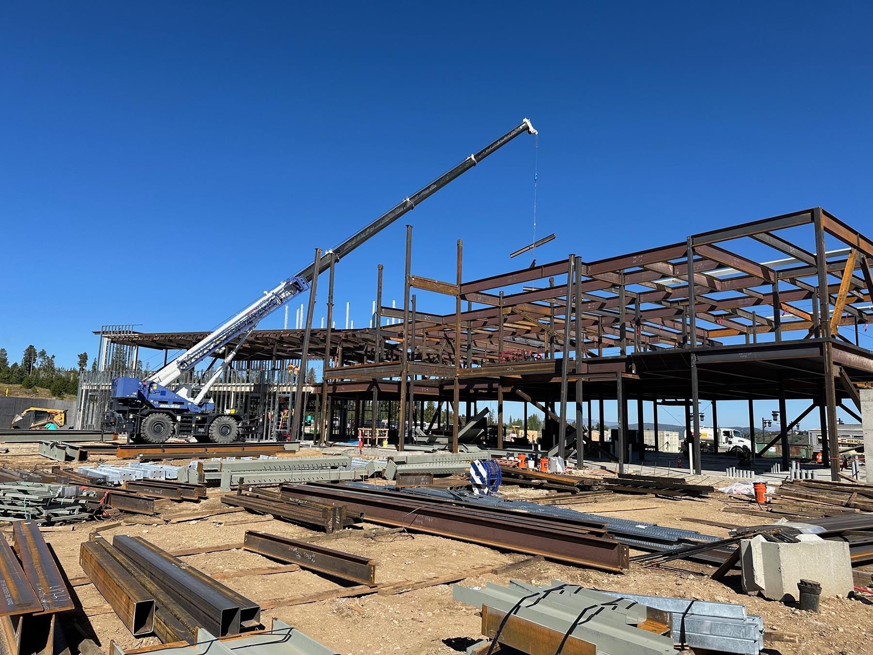 Construction site with steel-frame building and crane under a clear blue sky