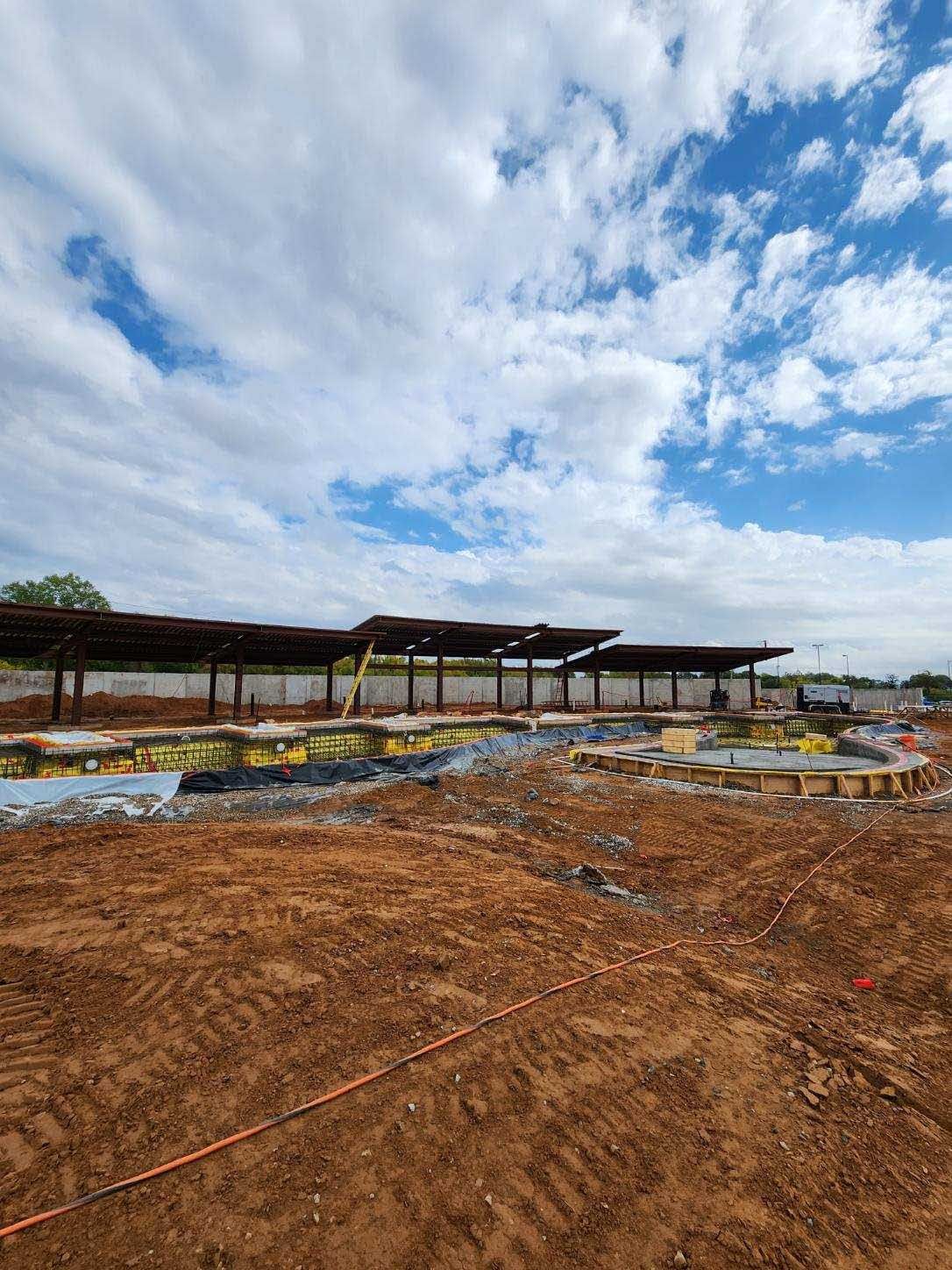 Muddy construction site with long roofed structures under a cloudy sky