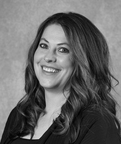 Smiling woman with long wavy hair in a dark top against a gray studio background