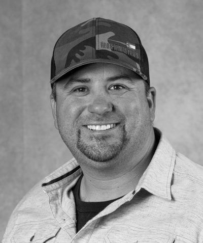 Smiling man in a baseball cap and collared shirt against a plain background