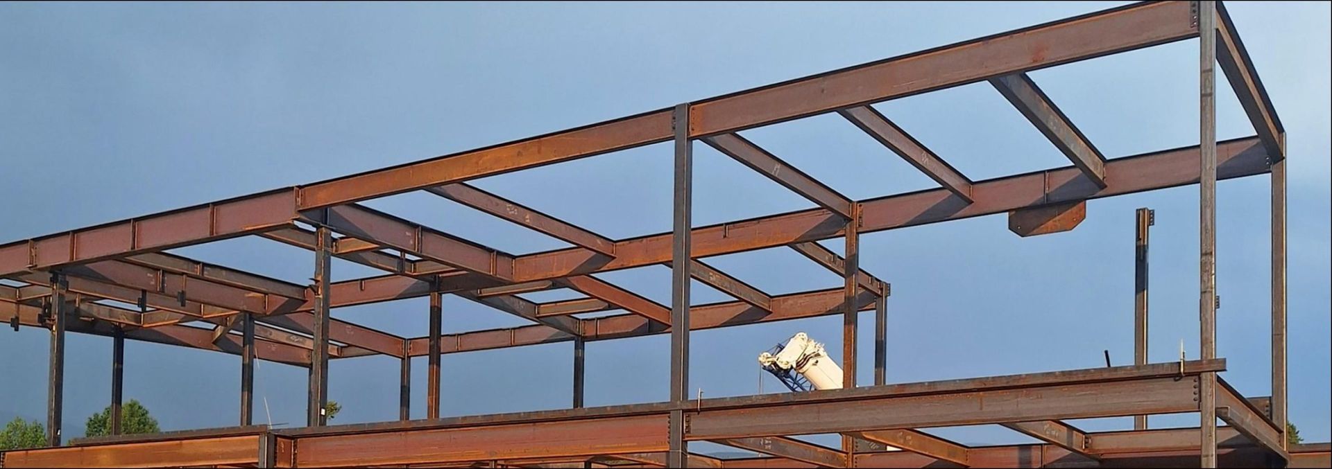 Steel framework of a building under construction, with a worker on an elevated platform against a clear sky.