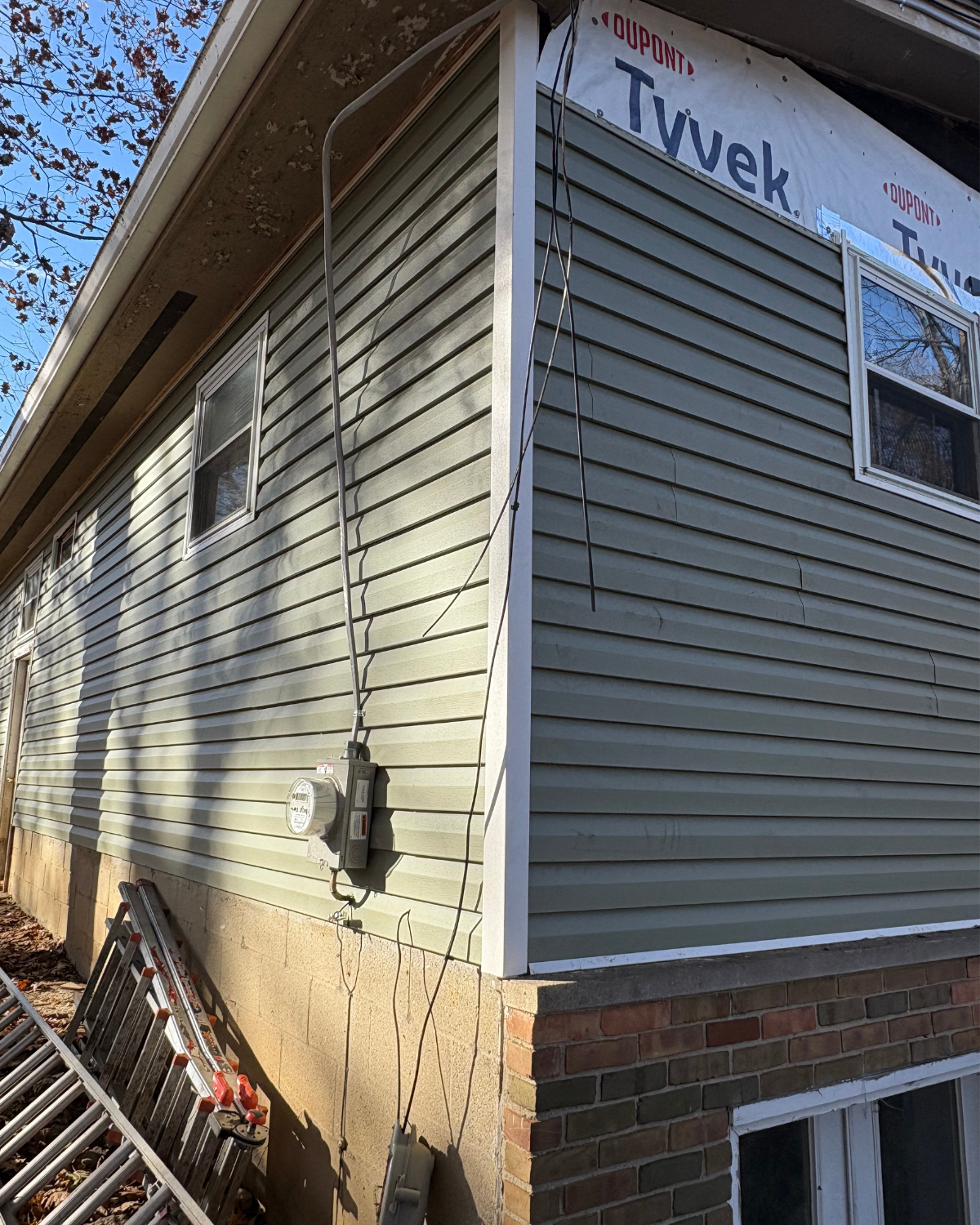 Exterior of house with green siding, exposed wiring, and Tyvek wrap.