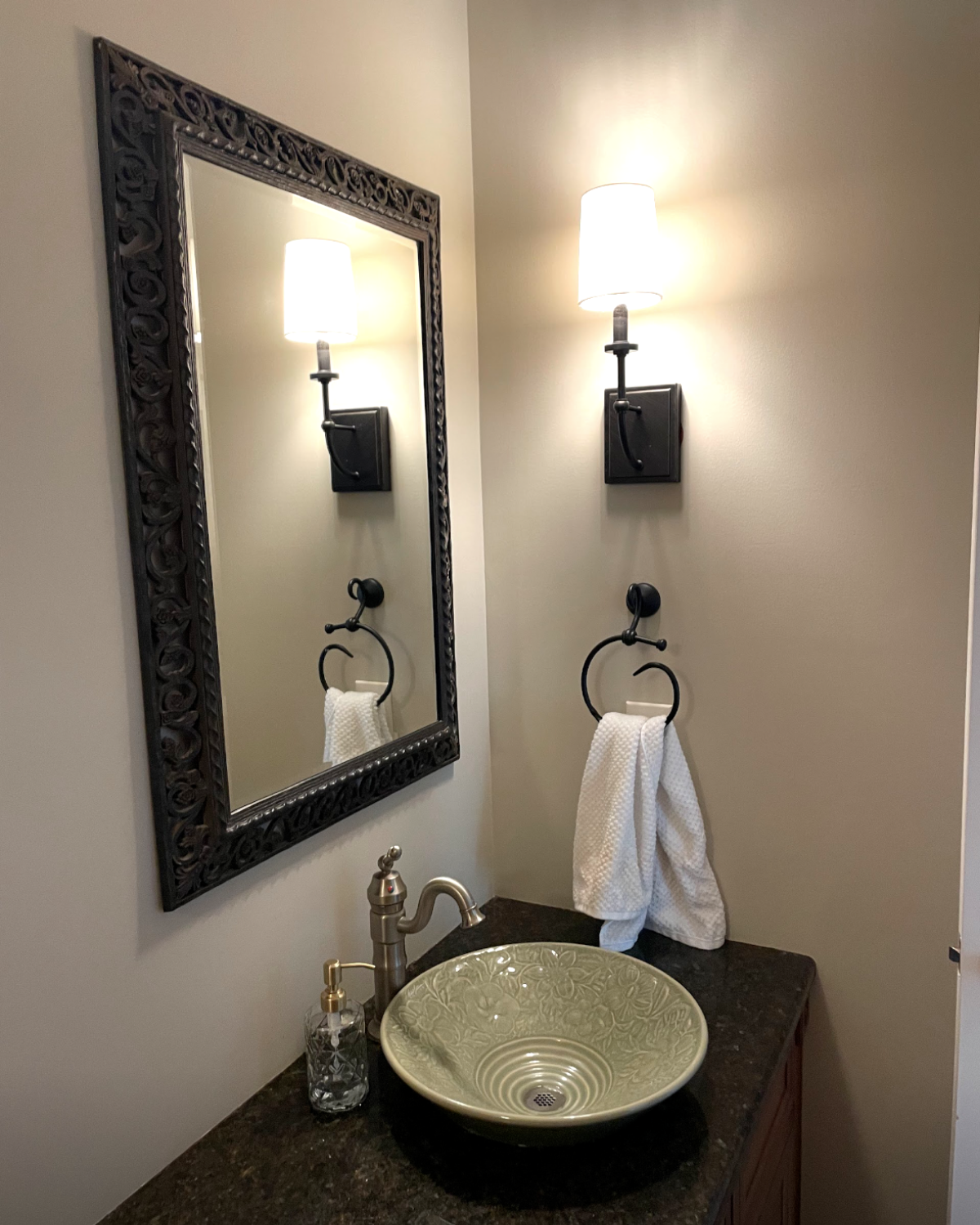 Bathroom with ornate mirror, sconce lights, vessel sink, and towel ring.