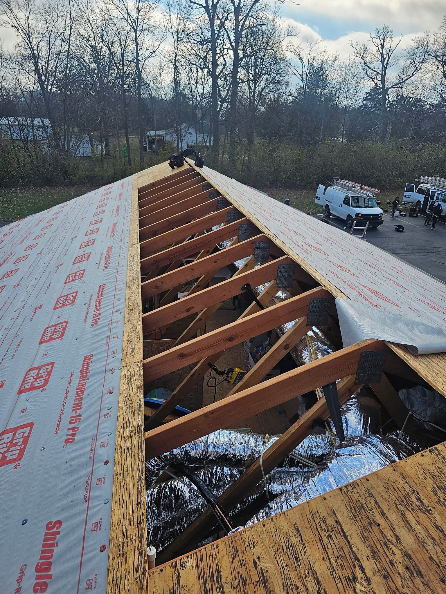 Roof under construction, showing rafters, insulation, and partially laid underlayment.