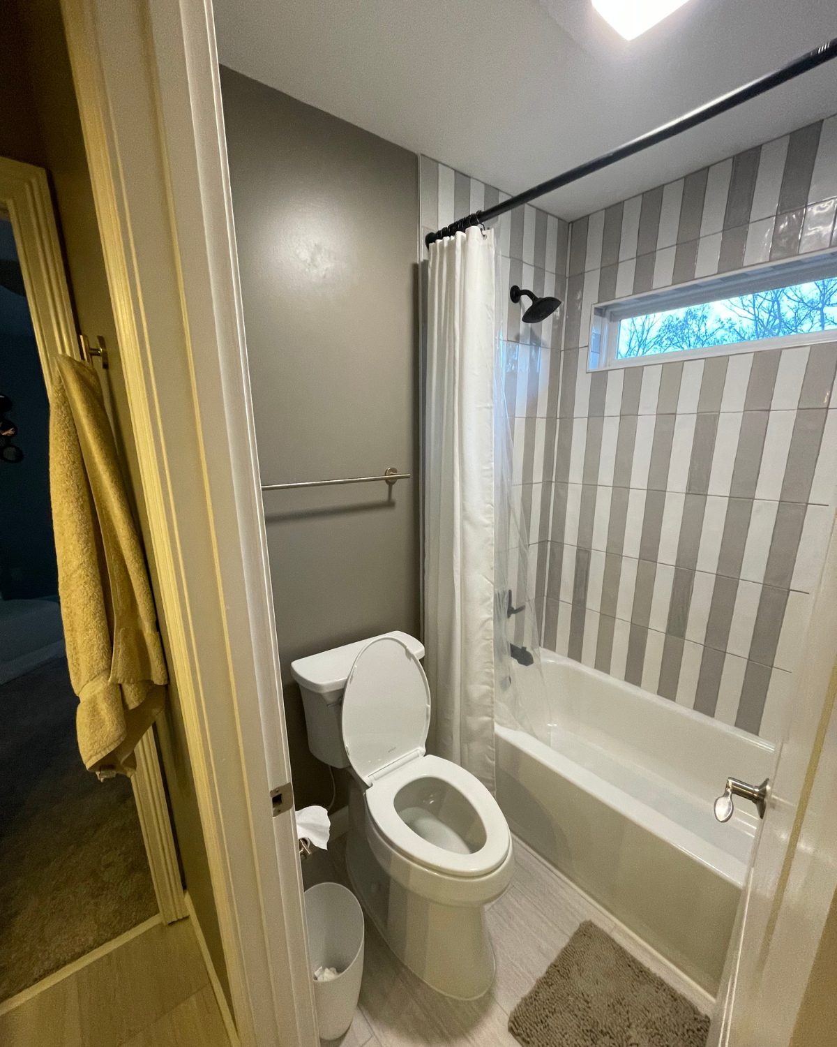 Bathroom with toilet, tub, and gray and white striped tile.