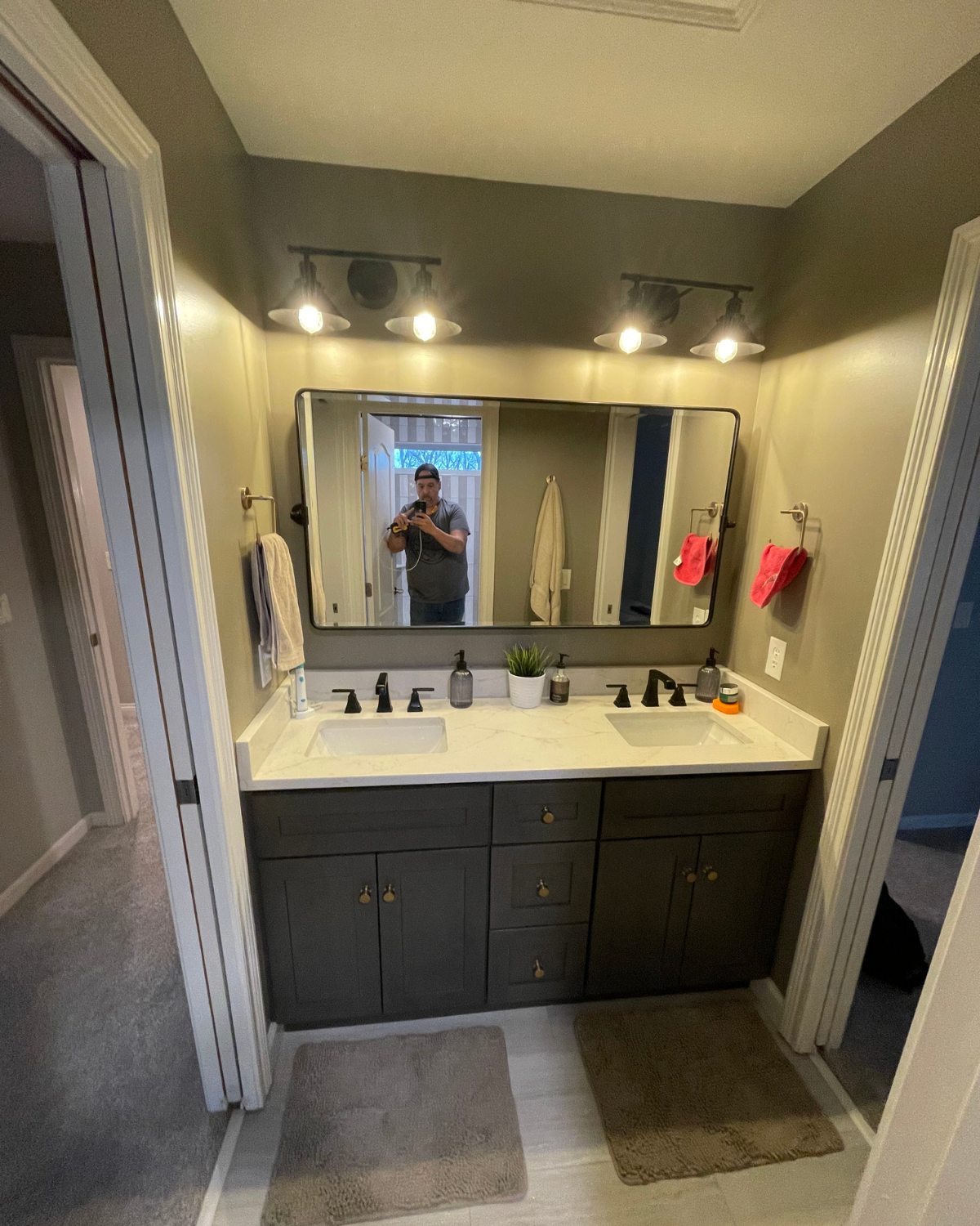 Bathroom with dark cabinets, white countertop, and large mirror. Two sinks, two light fixtures, and two rug mats.