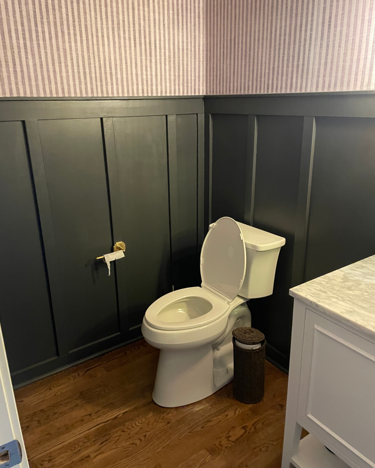 Bathroom with dark paneling, toilet, and wallpaper. Brown floor and white cabinet.