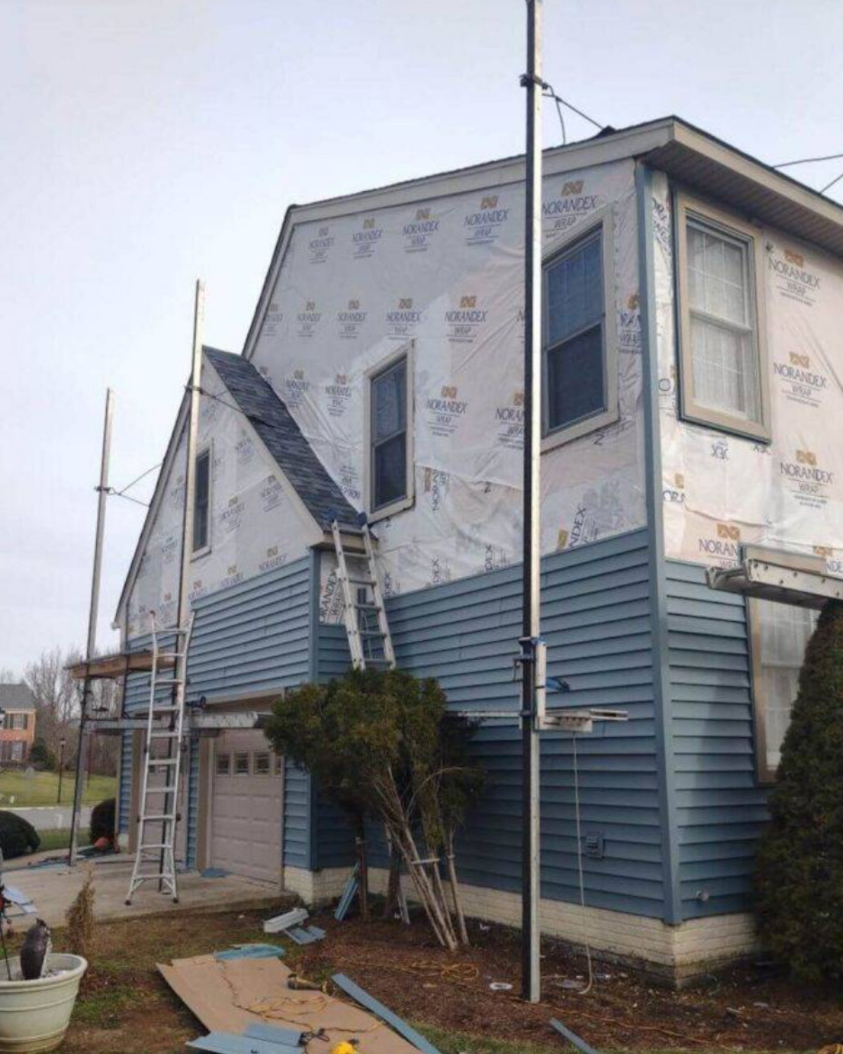 House under construction with blue siding, scaffolding, and a ladder against the side.