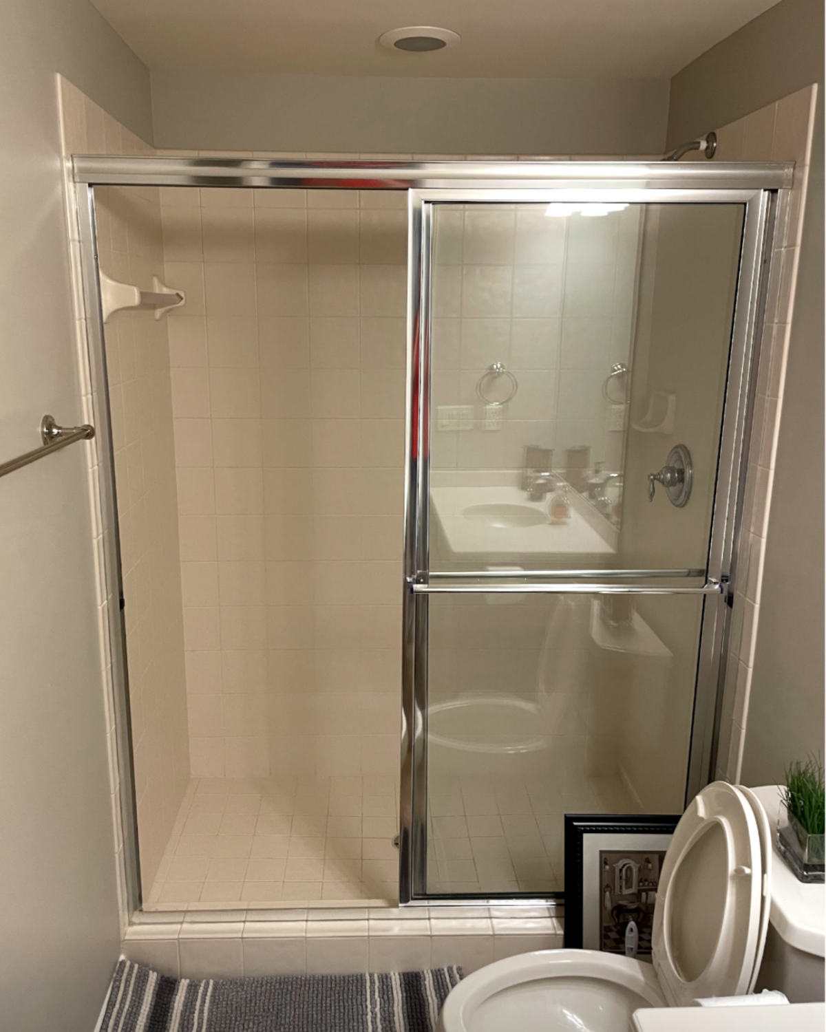 Shower stall with sliding glass doors, white tile, toilet, and sink visible.