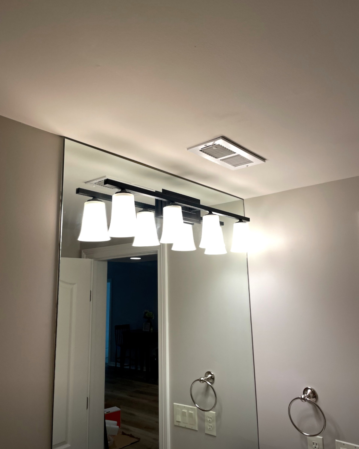 Bathroom with large mirror, black light fixture with six white lamps, and a ceiling vent.