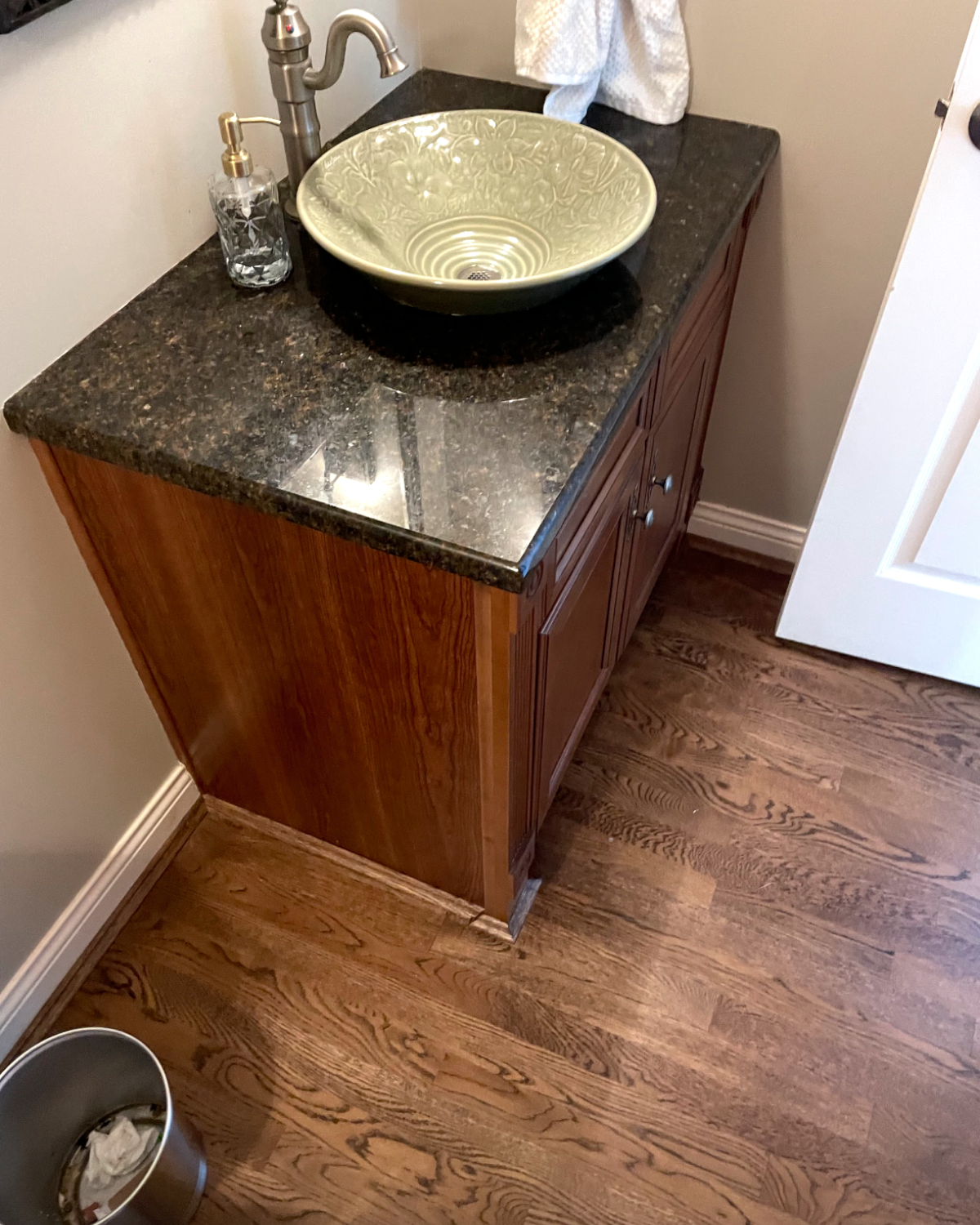 Vanity with dark granite countertop, vessel sink, and brown cabinet. Silver faucet, soap dispenser, and white towel.