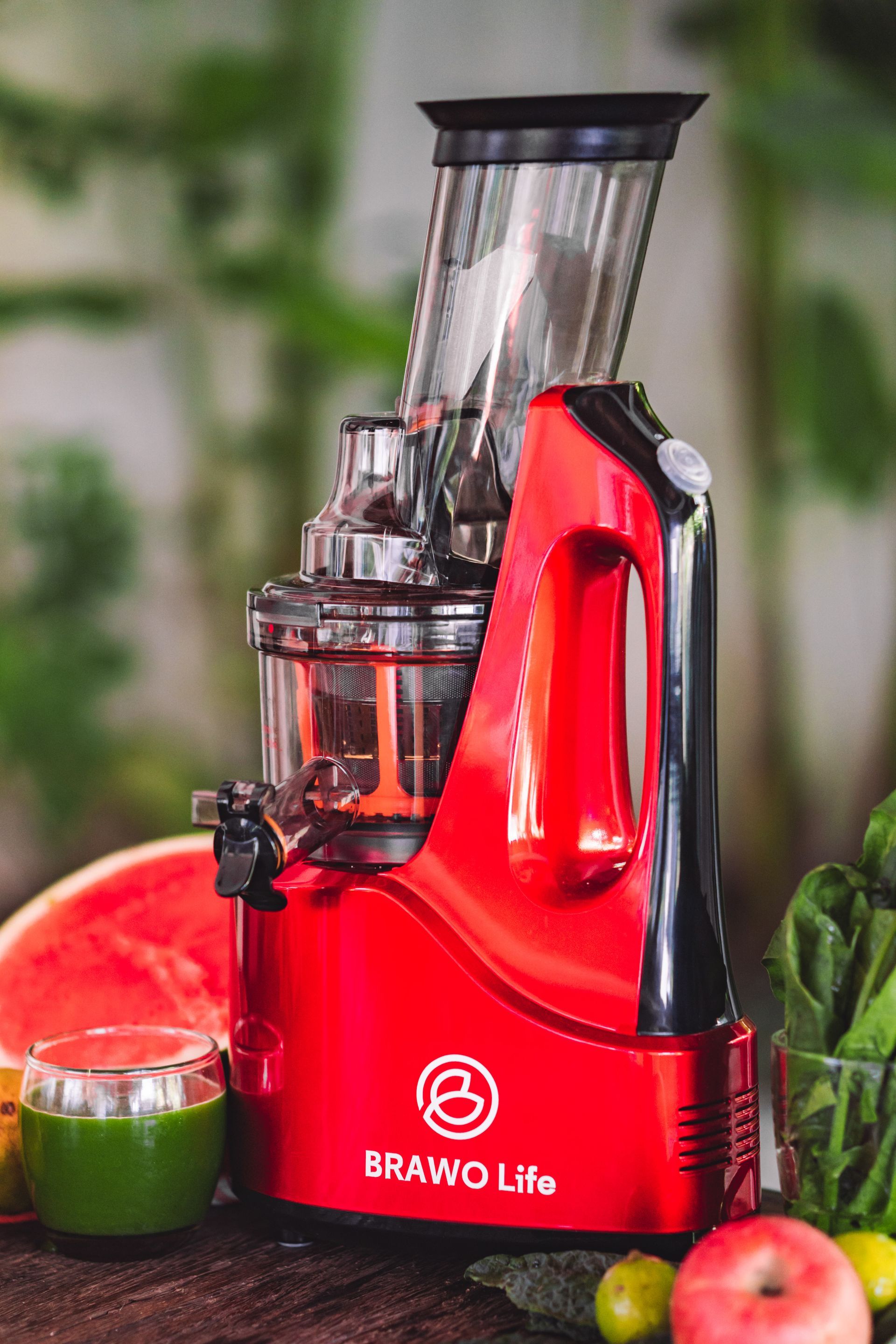 Pembuat jus Red Brawd Life dengan buah-buahan, gelas jus, dan tanaman hijau di latar belakang.
