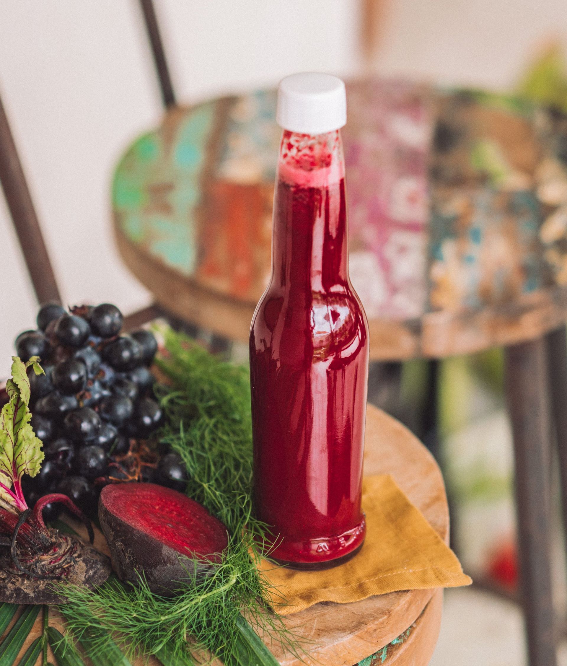 Sebotol jus bit, anggur, dan bit di atas bangku kayu; warna merah cerah.