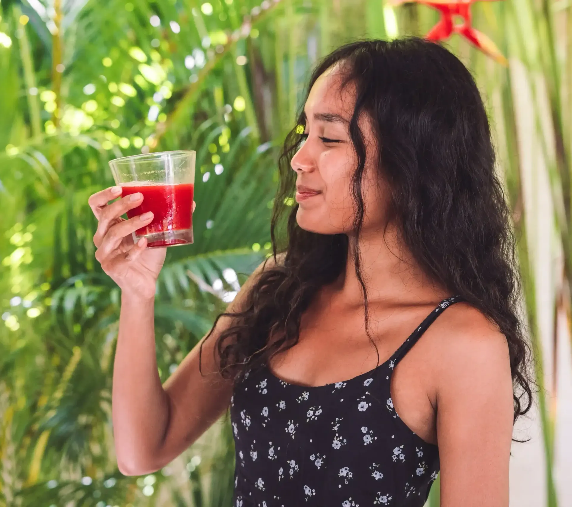 Wanita memegang dan mencium segelas jus merah di luar ruangan.