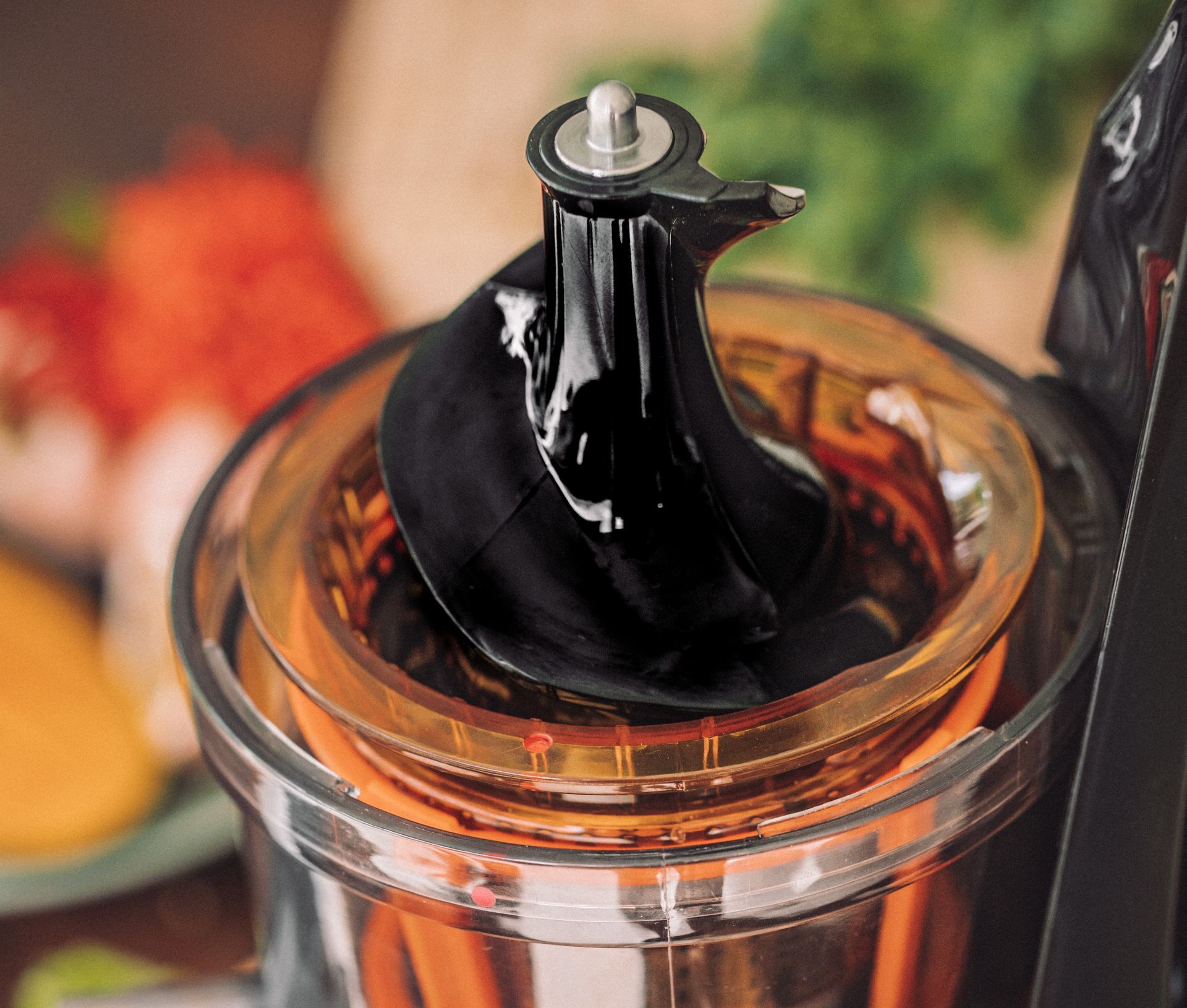 Tampilan dekat komponen interior juicer: auger hitam di dalam ruang bening dengan jaring oranye.
