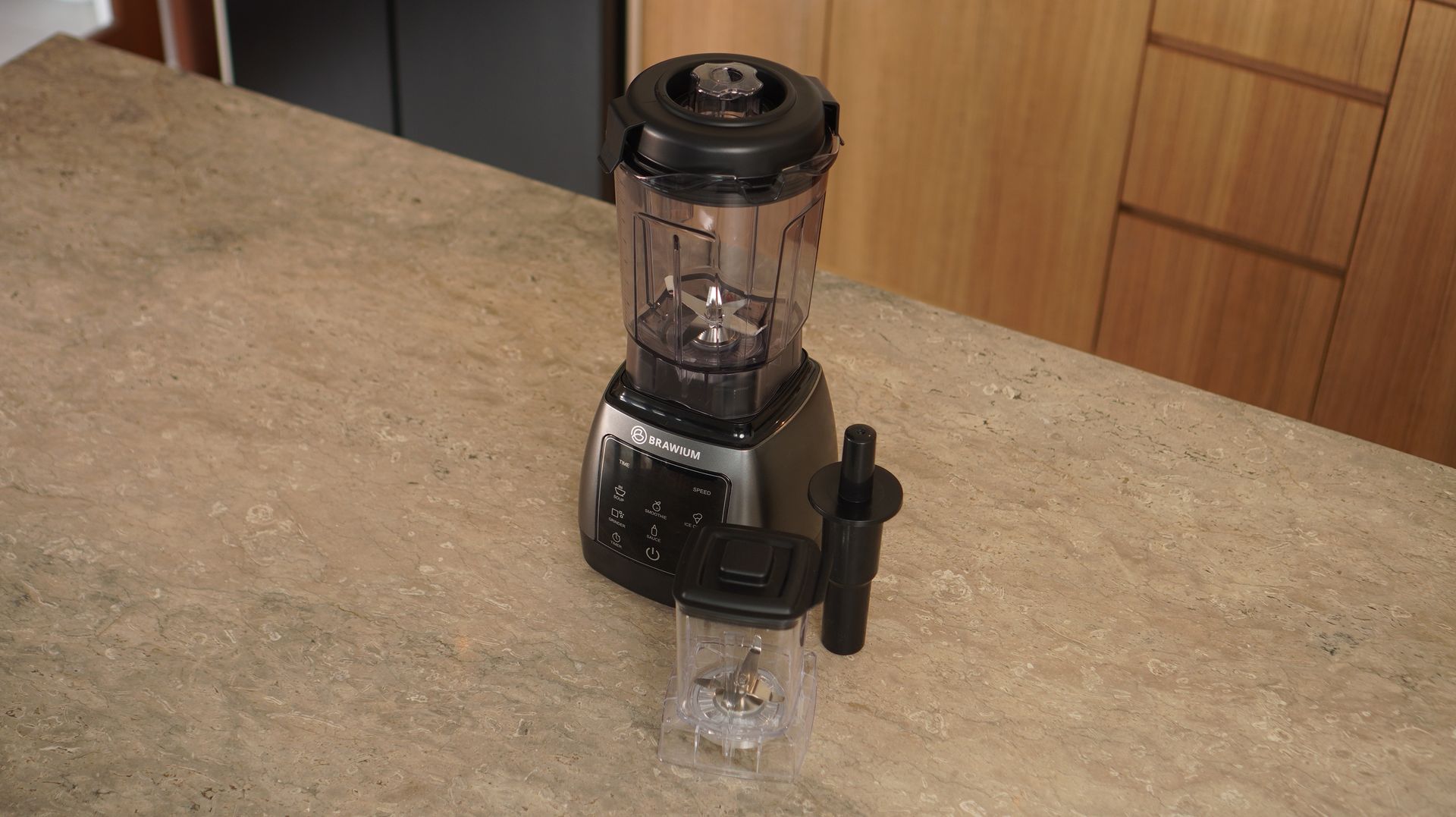 Blender hitam dengan wadah transparan di atas meja dapur berwarna krem.