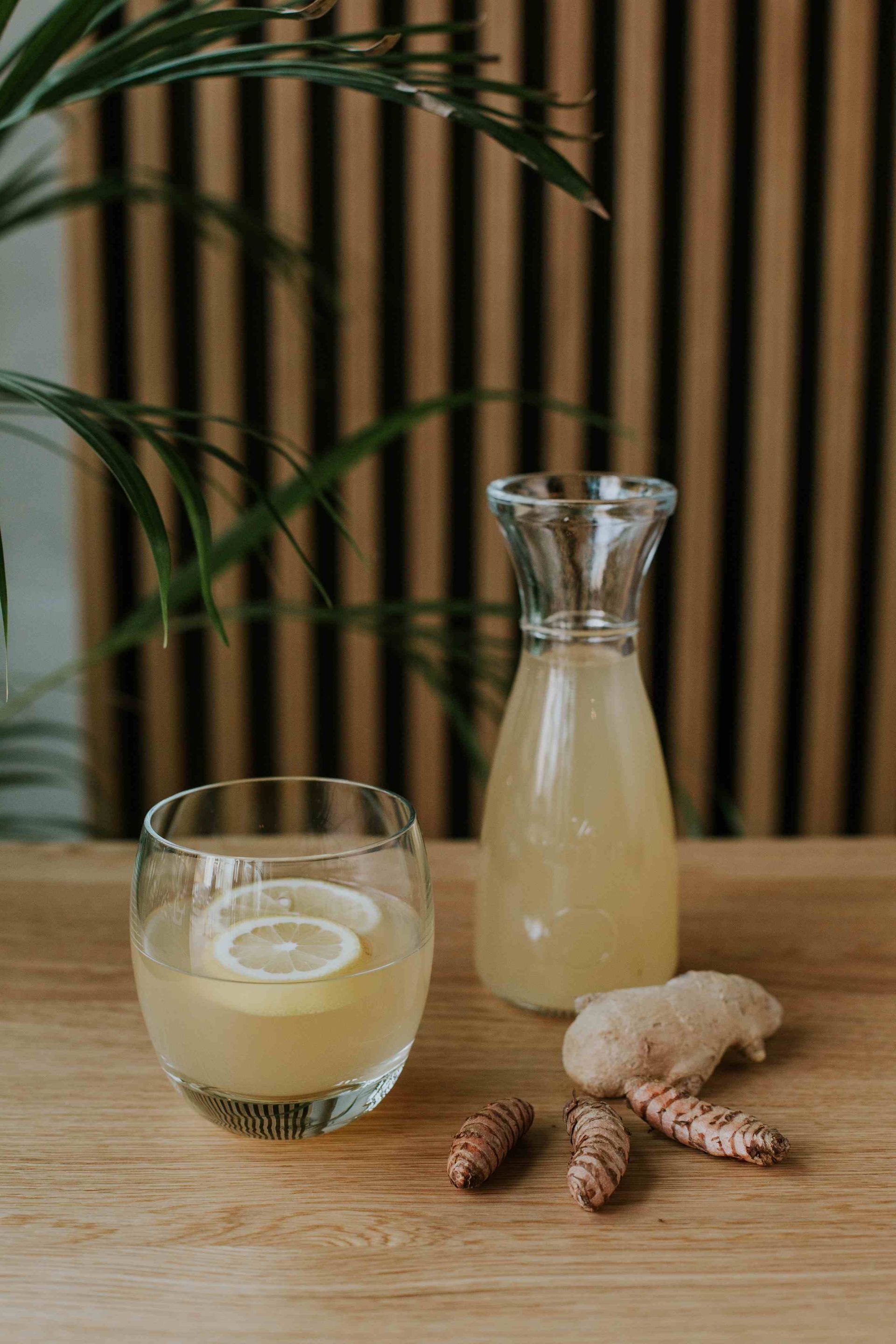 Jus hijau dalam gelas, dihiasi daun mint, dengan latar belakang sayuran dan buah.