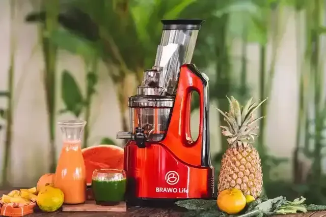 Pembuat jus merah dengan gelas buah dan jus di atas meja. Nanas dan daun hijau ada di sebelahnya.