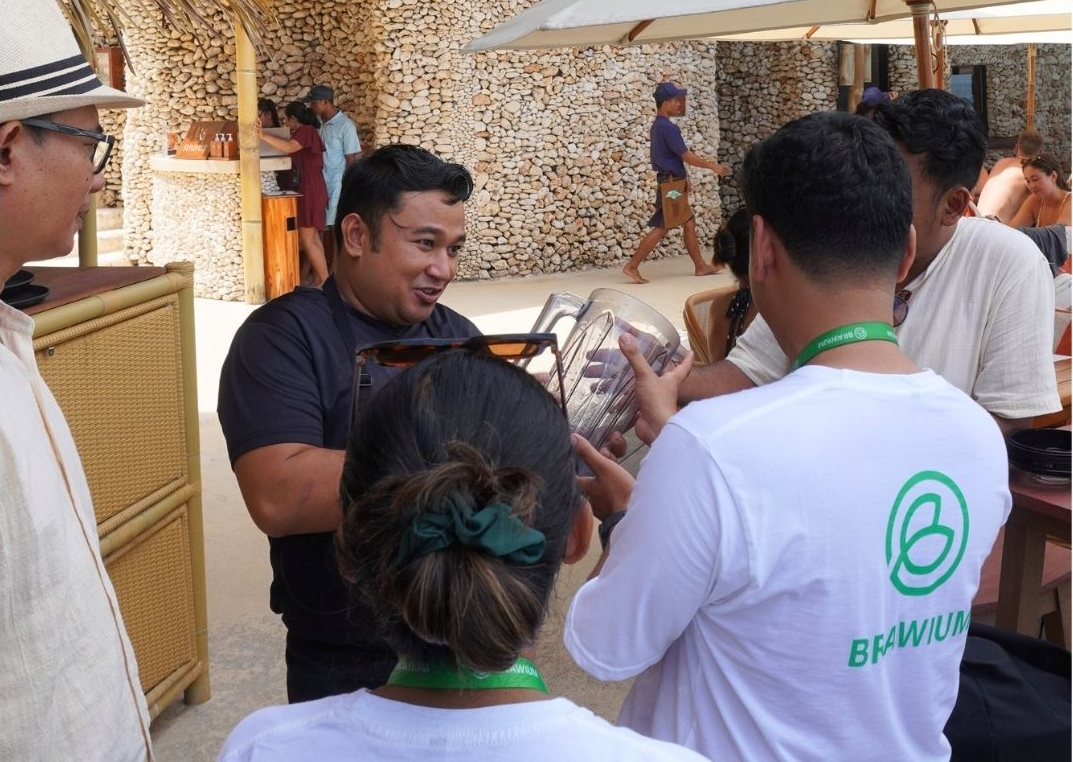 Sekelompok orang berinteraksi di luar ruangan, beberapa mengenakan tali gantungan. Seorang pria memegang benda bulat bening.