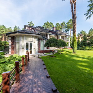 Modern house with curved brick walkway, manicured lawn, and tall trees on a sunny day