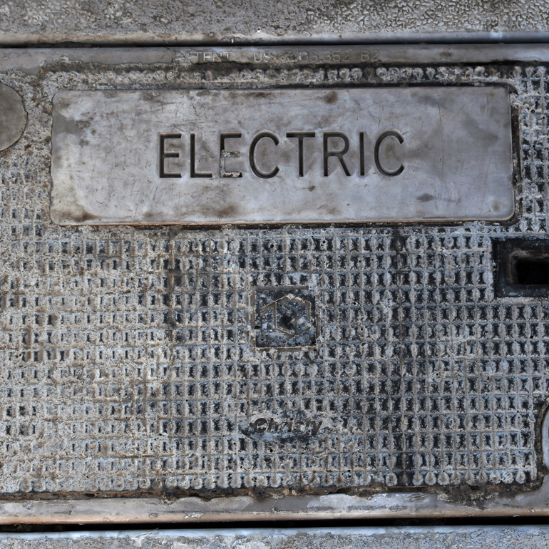 Metal utility cover labeled “ELECTRIC” on a gray concrete surface.