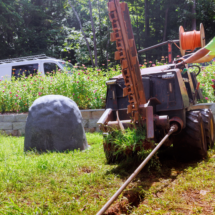 Tractor with a raised mower in a grassy yard beside a large gray rock and white van