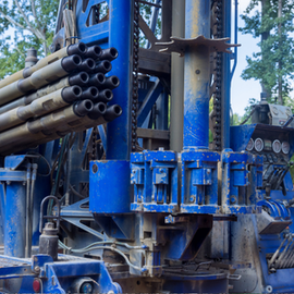 Blue drilling rig with stacked pipes and metal machinery in an outdoor industrial setting
